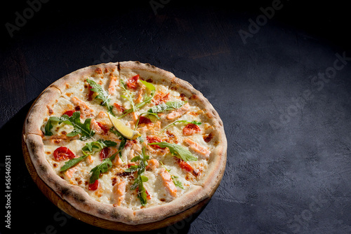 Pizza with salmon, mozzarella, cherry tomatoes, arugula, lemon and parmesan. Italian cuisine. On a black background. Free space for text. View from above.