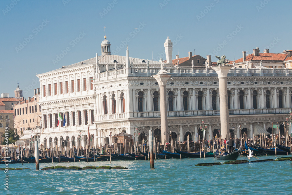 VENICE, ITALY - FEBRAURY 14, 2020: View on St. Marco square from water with Library, coloumns of St. Marco and St. Theodor, boats and gondolas on water.
