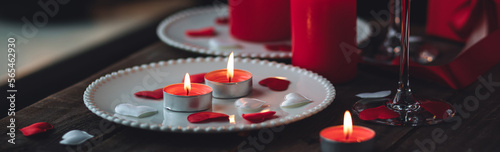 Saint Valentine s Day celebration. Red burning candles  hearts  gift box  postcard on dark wooden background. Happy holiday. Table decor for festive dinner  romantic atmosphere. Banner