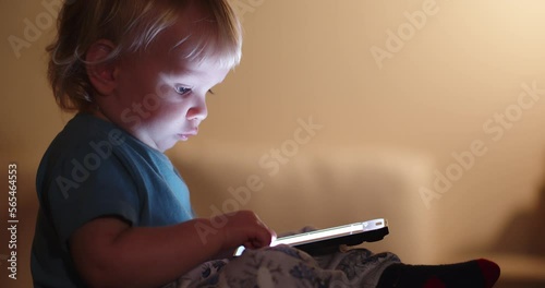 Little Child looking on mobile phone screen. Small child pressing with finger on phone touch screen. Light from the mobile phone screen illuminates the face of a small child. Cell phone and child