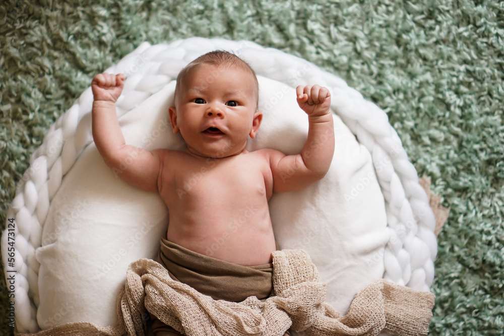 happy cheering naked newborn baby lying on a white round bed with arms