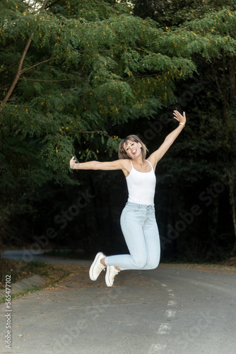 beautiful woman jumping on the road in the middle of a forest wearing jeans and white t-shirt
