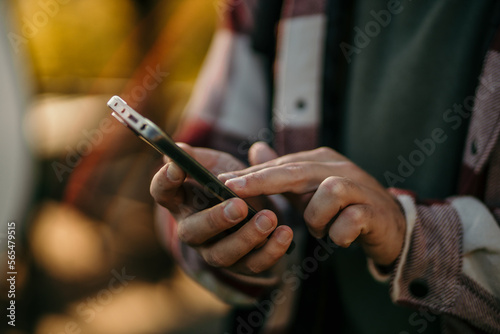 A young man sending messages from his cell phone  during hiking in mountains. Traveler man using a mobile phone application. Focus on the hand. Travel and lifestyle