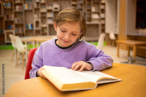 boy reading a book, doing homework while sitting at a table in a classroom or library	