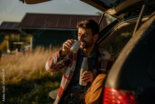 Photo of a young man, sitting in his car after hiking in nature and exploring, at sunset.