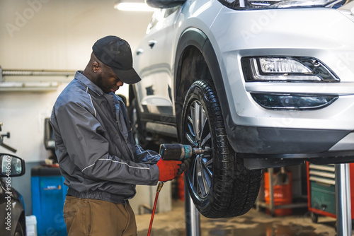 Mechanic changing tyres using an electric wrench car is lifted for a smooth process. High-quality photo