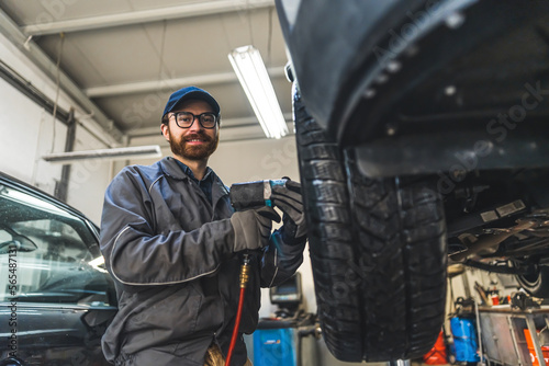 Mechanic changing tyres using an electric wrench car is lifted for a smooth process. High-quality photo