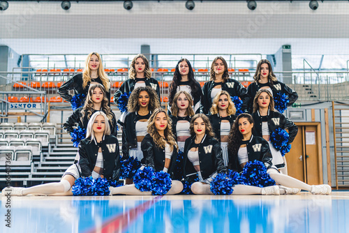 Front shot of a group of cheerleaders posing in their uniforms and blue pom-poms. High quality photo