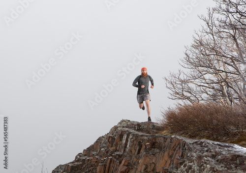 A trail male trail runner traverses a cliff face in the fog and snow. photo