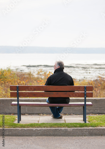 Rear view of mature man overlooking river in Autumn alone.