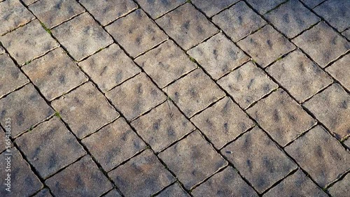 Stone tiles pavement made of granite or marble - pattern of brown floor paving as background. Texture of rough wavy uneven surface revealed by side lighting.