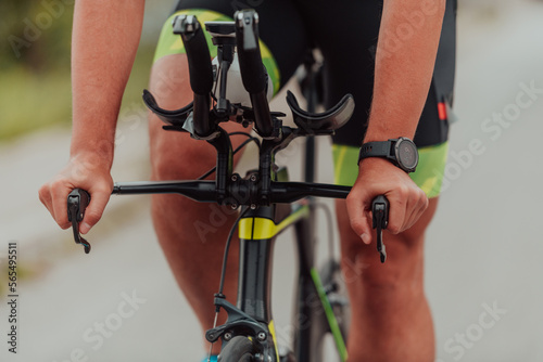 Fototapeta Naklejka Na Ścianę i Meble -  Close up photo of an active triathlete in sportswear and with a protective helmet riding a bicycle. Selective focus