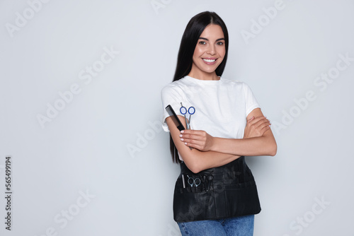 Portrait of happy hairdresser with professional scissors and comb on light background, space for text photo