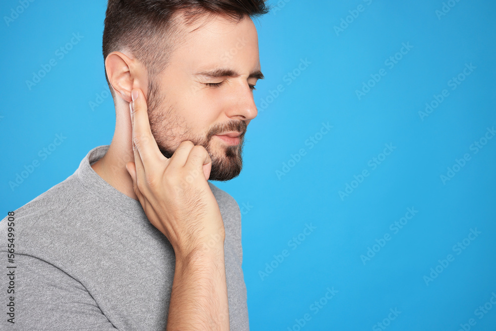 Young man suffering from ear pain on light blue background. Space for text Young man suffering from ear pain on light blue background. Space for text