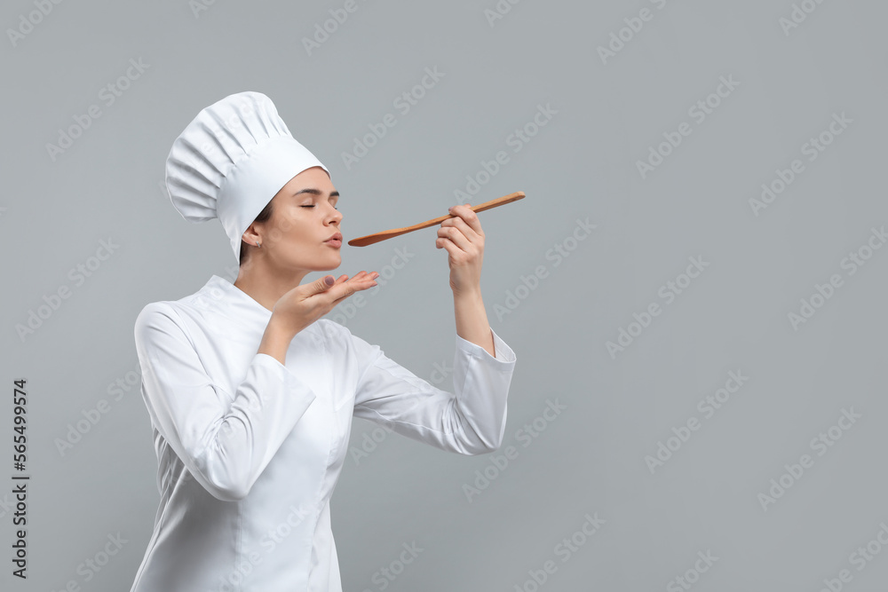 Happy female chef tasting something on light grey background. Space for text Happy female chef tasting something on light grey background. Space for text