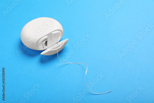 Container with dental floss on light blue background, closeup. Space for text
