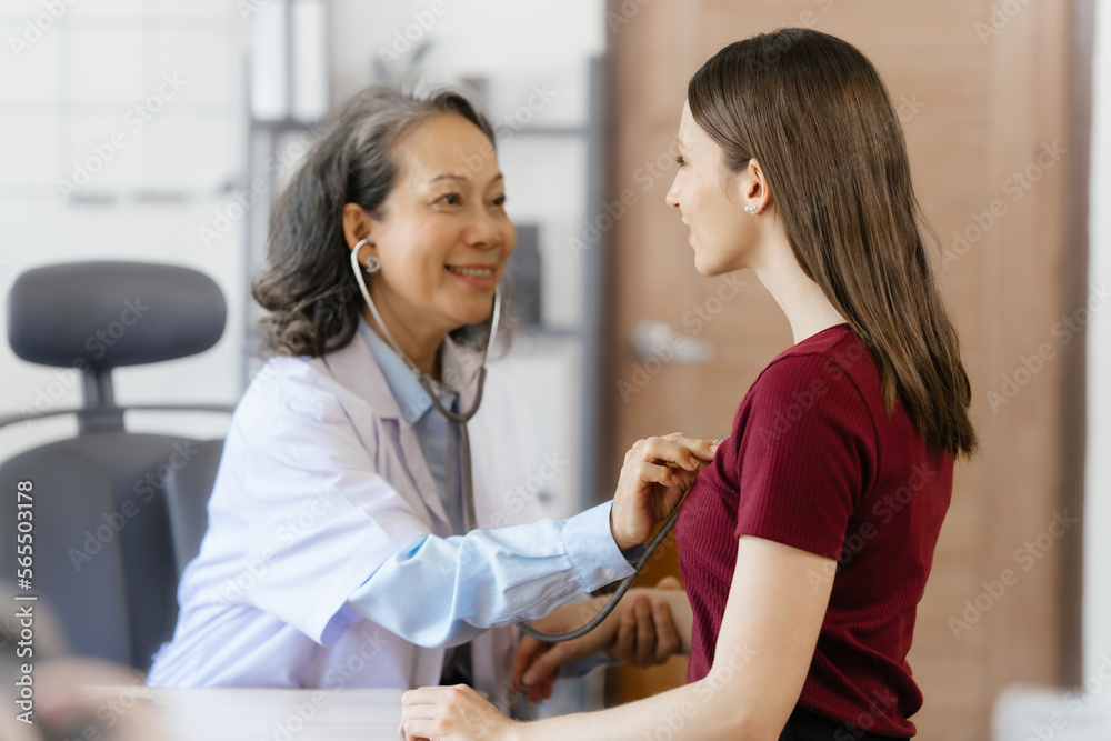 Fototapeta premium Female elder doctor takes a history of a patient and gives a consultation about osteopathy to a female patient after measuring blood pressure and heart rate and encouragement by holding hands