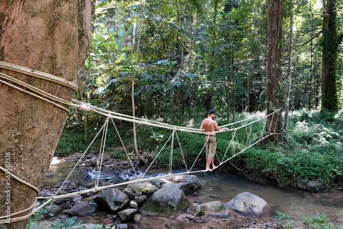 A tourist (middle aged man) crosses a creek in the jungle on a rope bridge on a sunny day. Khao Phanom Bencha National Park, Krabi Province, Thailand. photo