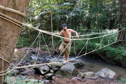 A tourist (middle aged man) on a rope bridge over a creek in the jungle on a sunny day. Khao Phanom Bencha National Park, Krabi Province, Thailand. photo