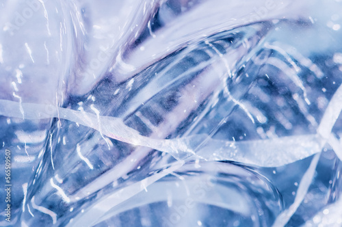 Bubbles and cracks inside natural ice. Abstract background. Geometric wavy pattern of glare and light distortion. Close up. Selective focus