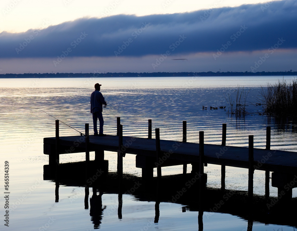 A Single Fisherman Stands on the Dock Fishing in Pre Dawn Light