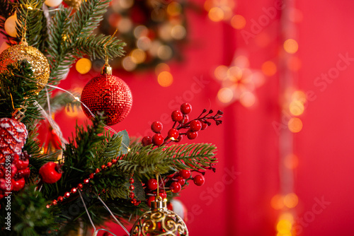 Close-up of a Christmas tree with decorations on a background of a red wall with a bokeh of yellow garlands.