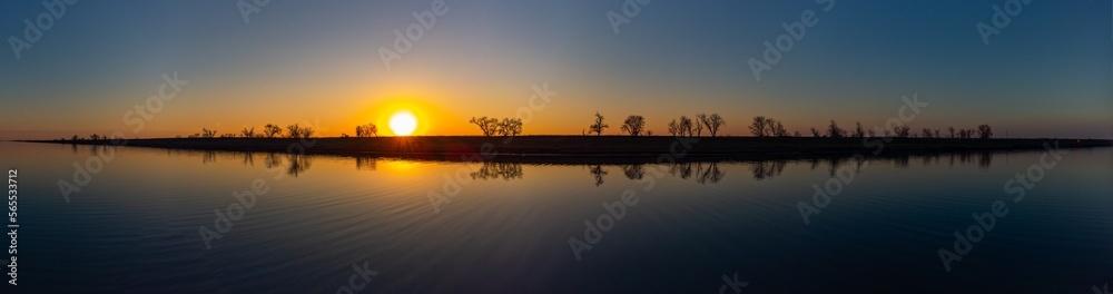 Panoramic landscape view of trees reflecting on river at sunset in winter 