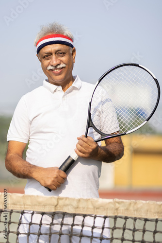 Portrait of smiling senior man holding tennis racket. © G-images