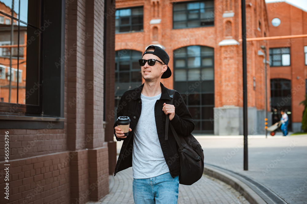 Portrait of a stylish hipster guy in sunglasses with a backpack in the city against the background of a modern city building.