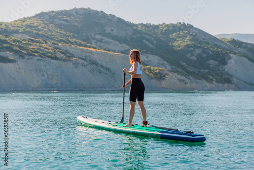Young woman rowing on stand up paddle board at quiet sea with beautiful landscape.