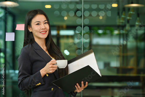 Happy Mature businesswoman holding a cup of coffee with a folder at office room.