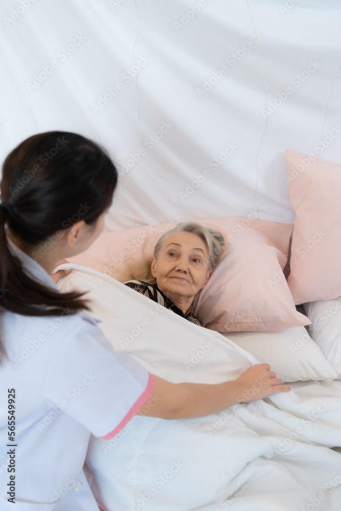 Caregiver for an elderly woman blanket the elderly woman on the bed After completing the weekly health check-up at the patient's home Caregiver for an elderly woman blanket the elderly woman on the bed After completing the weekly health check-up at the patient's home