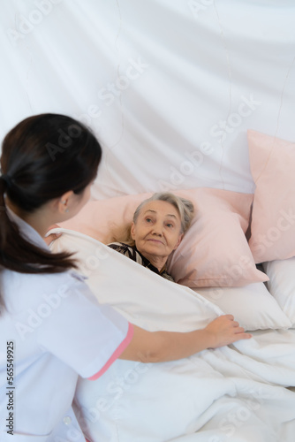 Caregiver for an elderly woman blanket the elderly woman on the bed After completing the weekly health check-up at the patient's home