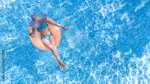 Beautiful woman in hat in swimming pool aerial top view from above, young girl in bikini relaxes and swims on inflatable ring donut and has fun in water on tropical vacation on holiday resort 