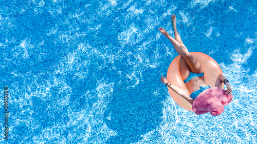 Beautiful woman in hat in swimming pool aerial top view from above, young girl in bikini relaxes and swims on inflatable ring donut and has fun in water on tropical vacation on holiday resort 