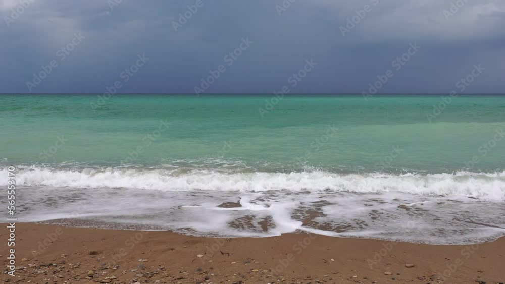 Overcast sky on rainy day with foamy waves rolling towards golden sand beach under low warm sun light. Nobody. Holiday recreation concept. Abstract nautical summer ocean sunset nature. Overcast sky on rainy day with foamy waves rolling towards golden sand beach under low warm sun light. Nobody. Holiday recreation concept. Abstract nautical summer ocean sunset nature.