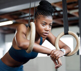 Black woman, fitness and gymnastics with rings for training, muscle and arms at gym. African American female acrobat or gymnast face in strong focus for exercise, workout or practice at the gymnasium