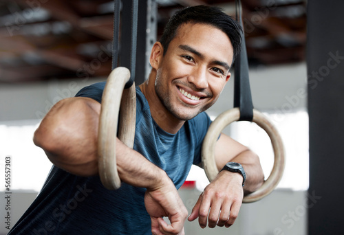 Portrait, gymnastic rings and olympics with a man gymnast hanging on equipment for workout in gym. Face, fitness and exercise with a male athlete training in gymnastics for health or power