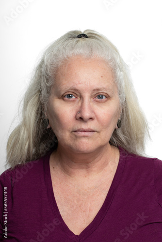 Older middle aged woman with long gray or grey hair on white background looking ahead at camera with stern grouchy expression