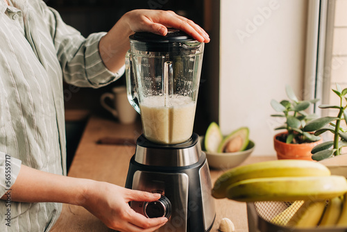 Woman blending spinach, berries, bananas and almond milk to make a healthy green smoothie