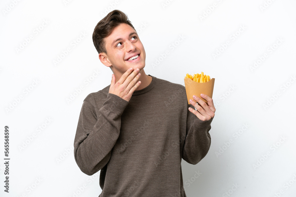 Young Brazilian man holding fried chips isolated on white background looking up while smiling Young Brazilian man holding fried chips isolated on white background looking up while smiling