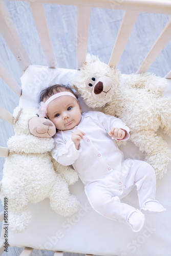 cute baby girl with teddy bears on the bed on a white cotton bed, falling asleep or waking up in the morning, funny newborn little baby at home in the crib close-up
