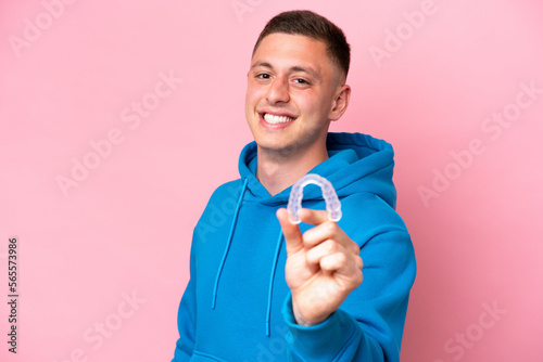 Young Brazilian man holding invisible braces isolated on pink background with happy expression