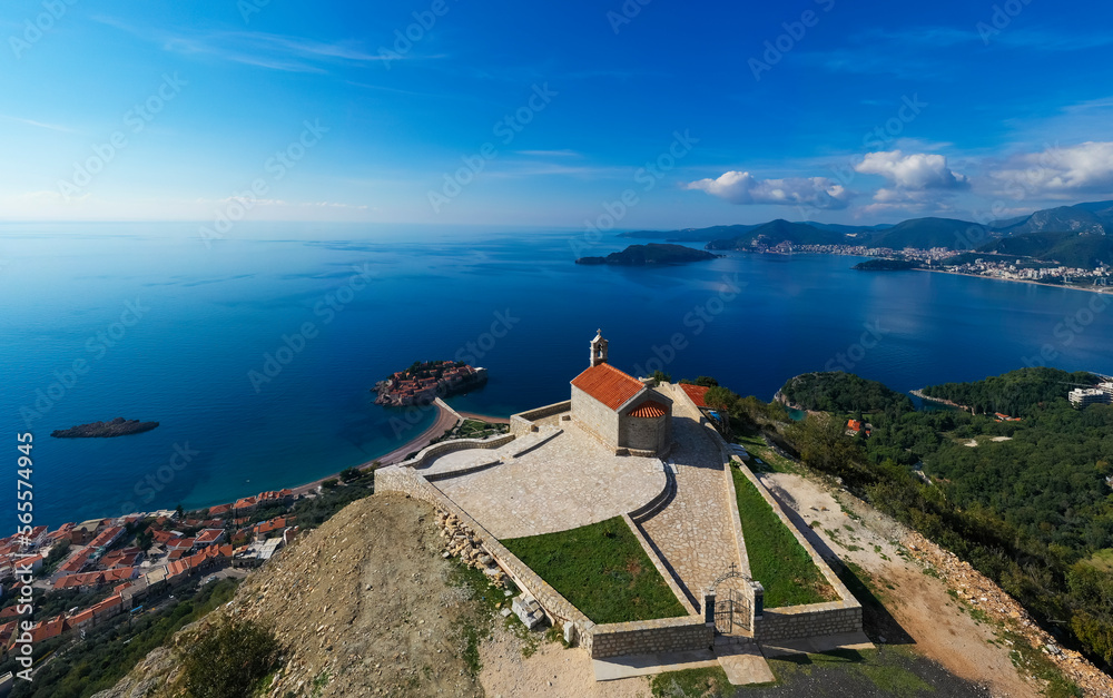 Aerial view of Sveti Stefan of Montenegro from Sava church, landmark of country from top with blue sea and rooftops of houses