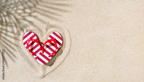 Fotografi Pare of red flip-flops in shape of heart on sand with palm leaves shadow, copy s