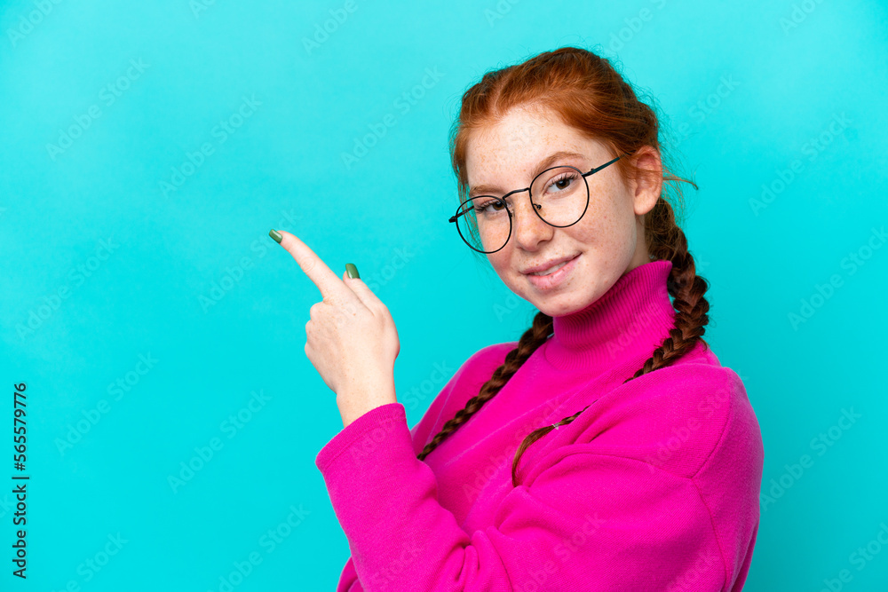 Young reddish woman isolated on blue background With glasses and pointing side Young reddish woman isolated on blue background With glasses and pointing side