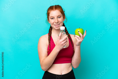 Young reddish woman isolated on blue background with an apple and with a bottle of water