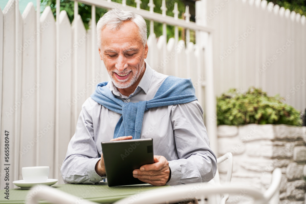 Handsome senior man working with tablet device in a bar outdoors Handsome senior man working with tablet device in a bar outdoors