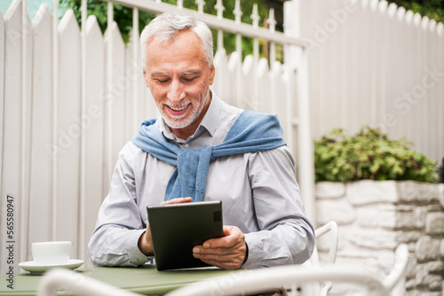 Handsome senior man working with tablet device in a bar outdoors