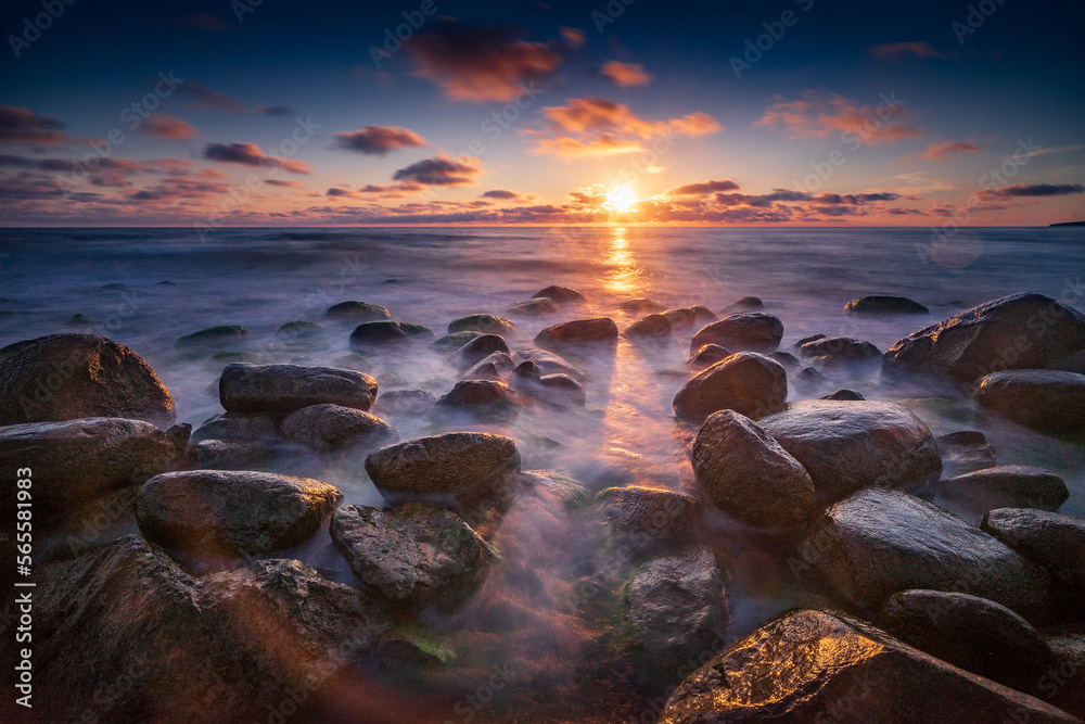 Boulders, shore, evening light, sunset, clouds, blue sky and rainbow on the Baltic Sea in Latvia, Europe. Calm blue see and big stones on the beach.